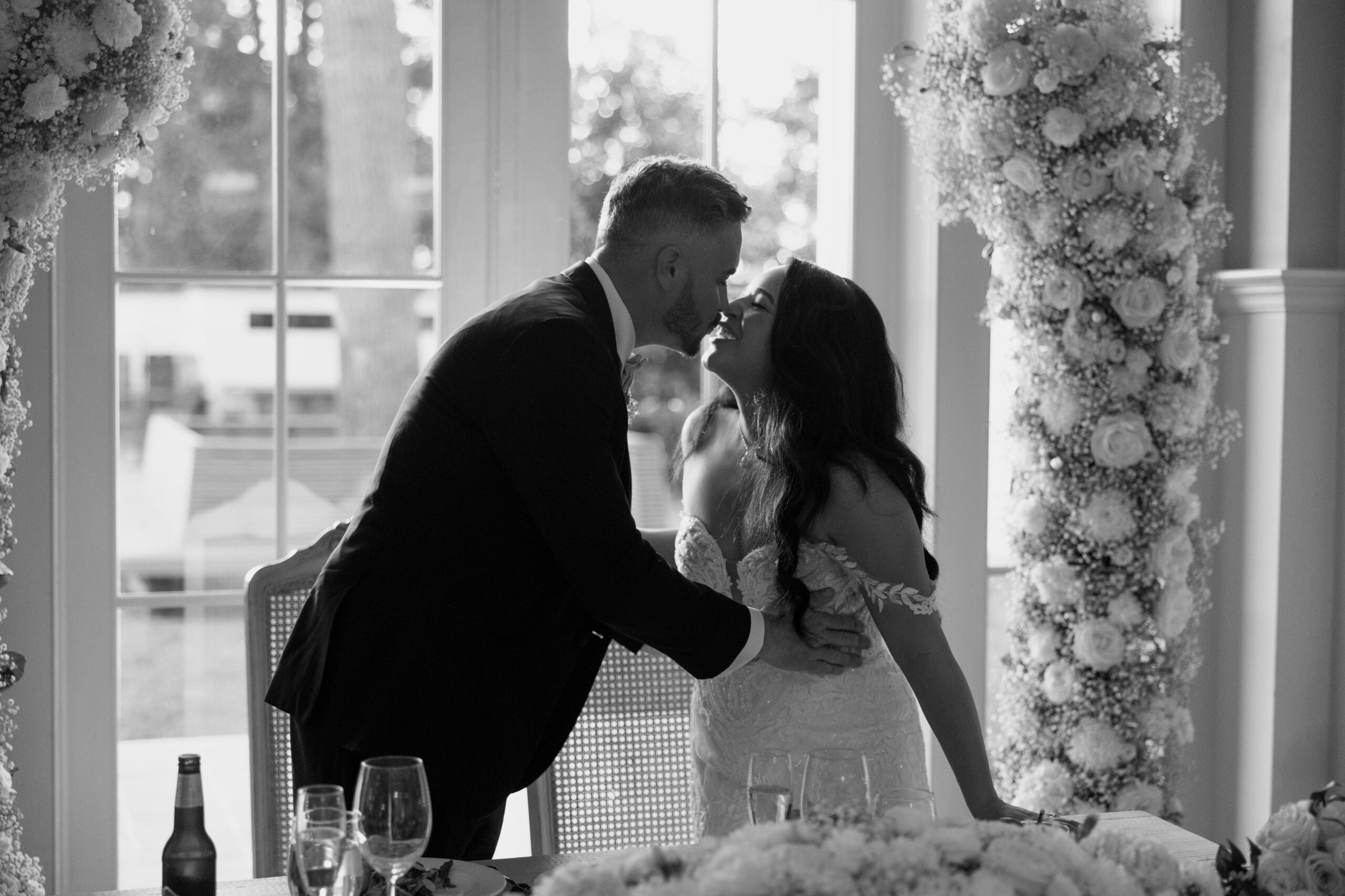 Black and white photo of bride and groom kissing at sweetheart table